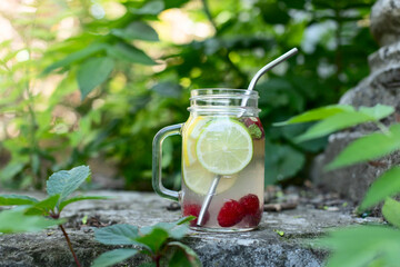 Lemonade with lemon, lime, raspberry and mint leaves in a glass mug with a metal tube outdoors on the street.