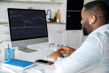 Investments, trading on the stock exchange. African american man trader investor, is analysing cryptocurrency financial market, looks at computer,trading data index chart graph on pc screen