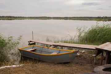 A wooden boat stands on the shore of the lake next to a wooden pier.