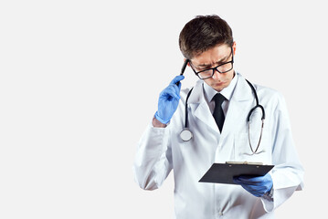 Fototapeta premium Doctor with a stethoscope on a white background. A man in a medical gown with glasses. The doctor is surprised with a tablet in his hands.