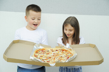 Cute girl and a boy eating a big delicious pizza outdoors
