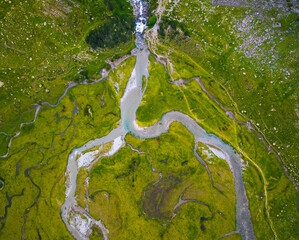 Aerial vertical drone view of a river flowing through a green valley.
