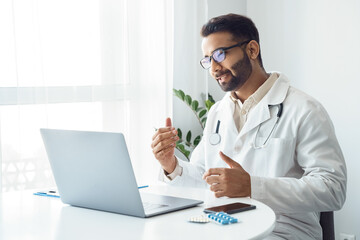 Portrait of indian man doctor talking to online patient on laptop screen
