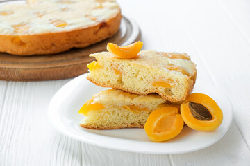 Piece of apricot sponge cake on plate with full cake and apricot fruits on background. Easy recipe of summer pie for tea time. Healthy nutrition, vegan dessert, gluten-off, sugar free.