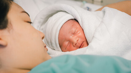 Young mother holding her newborn baby who sleep first days of life at hospital, love and Mother’s Day concept.