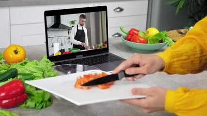 Housewife in kitchen knives sliced tomato from cutting board into salad bowl, study online cooking lesson. Man chef food blogger in laptop screen slices tomato tells teaches woman video call computer
