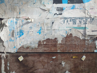 Fototapeta premium Abstract wooden wall background with peeled pieces of paper. Old grunge moldy stained paper on the wall. Old Facade with deteriorated wooden sheets and torn pieces of paper.