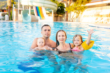 Fototapeta premium happy family mom, dad and two children are swimming in the pool with water slides and having fun on vacation, smiling and laughing