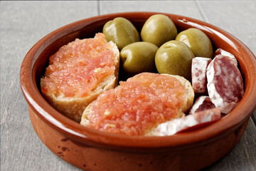 Simple tapas bowl with bread with tomato, olives and fuet.