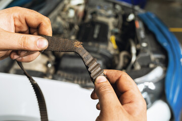 An auto mechanic shows a torn timing belt with worn teeth against the background of an open car...