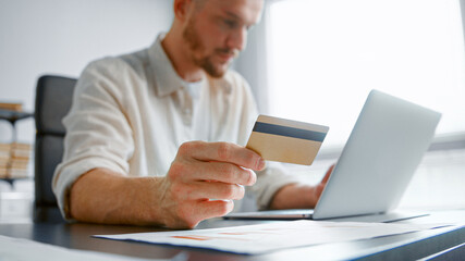 Blurred company accountant enters info via white laptop holding yellow bank card