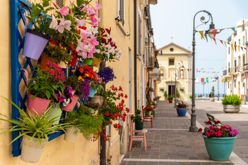 Fototapeta na wymiar June 2021, San Vito Chietino, Italy. Main square of San Vito Chietino, old colored chairs next to the entrance doors of the houses, for tired travelers and to support flower pots.