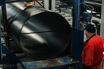 a worker of a pipe-rolling plant. conveyor line of the ferrous metallurgy enterprise. a worker in a uniform is engaged in metal welding