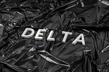 the word delta laid with silver metal letters on crumpled black plastic bag background in diagonal...