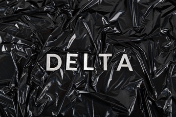 the word delta laid with silver metal letters on crumpled black plastic bag background