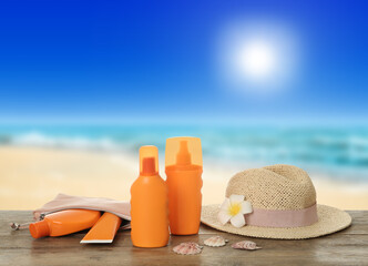 Fototapeta na wymiar Different skin sun protection products and hat on wooden table against seascape. Space for design
