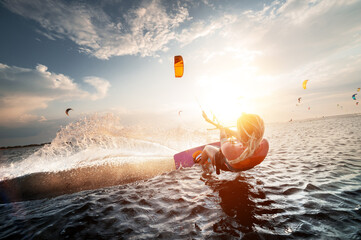 Professional kite surfer woman rides on a board with a plank in her hands on a leman lake with sea water at sunset. Water splashes and sun glare. Water sports - obrazy, fototapety, plakaty