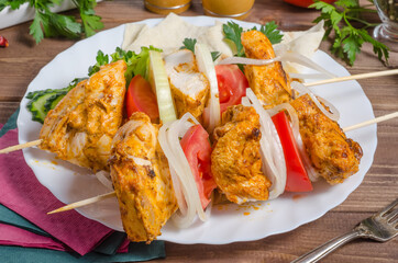Chicken kebab with onions on a white plate close-up