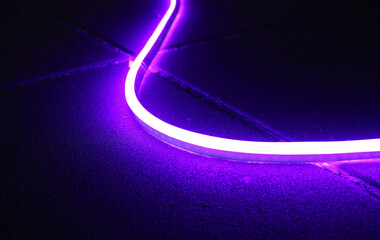 Purple led neon flexible strip light glowing on the floor in dark light.