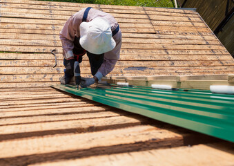 Construction elderly worker install new roof, Roofing tools, Electric drill used on new roofs with Metal Sheet. Self-made house by retired man.