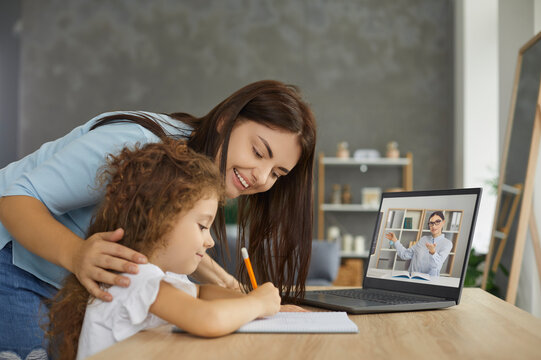 Kids Learning Online. Mum And Little Child Sitting At Table At Home, Watching Web Tutorial On Screen Of Laptop Computer, Doing Homework With Help Of Private Tutor Or Having Class With School Teacher