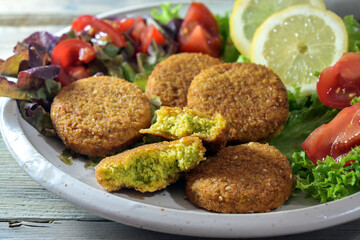 Vegetarian falafel from spiced chickpeas with salad of lettuce, tomatoes and lemon slices on a plate, close up shot, selected focus