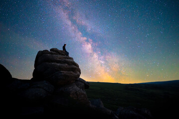 Figure stargazing atop rocks beneath the Milky Way, Dartmoor National Park, UK