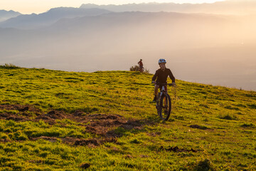 Fototapeta na wymiar Girl child riding mountain bike into the sunset. Beautiful golden summer light.