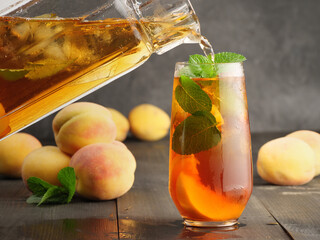 Peach ice tea with mint and ice on a dark wooden background.