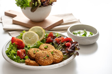 Fresh vegetarian falafel from chickpeas, sesame seeds, spices and herbs, served with salad and a yogurt dip on a white table, copy space, selected focus