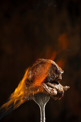 Tasty beef steak on a fork  with fire flames, smoke and salt on dark background. Freeze motion barbecue concept. Close up macro view on meat, copy space. Juicy grilled piece of meat.