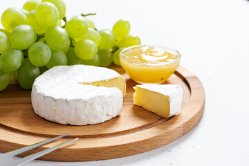 Sliced Camembert with fork on wooden cheese platter on white