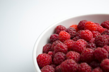 On a white background, on a large dish, a ripe and fragrant raspberry lies on a slide.