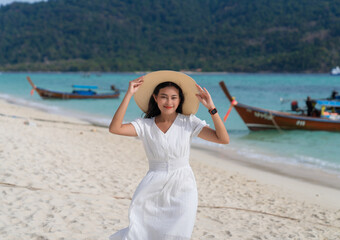 portrait of attractive Asian woman in white dress and wide brim hat smiling with happiness on blue sea beach at Lipe islands, Satun, Thailand, girl relax on vacation in summer