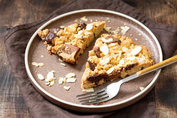 Two pieces of homemade shortbread pie with milk and bitter chocolate and almonds in a plate on a brown table close-up. Delicious sweet pastries