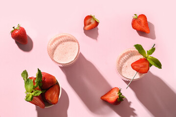 Indian lassi or strawberry milkshake on pink paper background with sunny shadow. View from above.