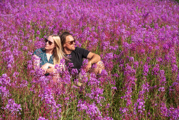 Two people, couple sitting in a field of Fireweed flowers during summertime in northern Canada, Yukon Territory. 