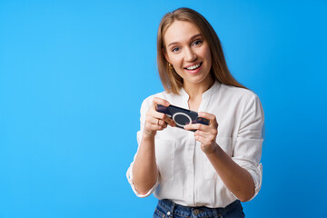 Positive young woman playing games on smartphone against blue background