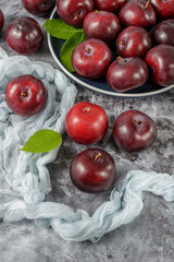 Fresh ripe purple plum fruits and leaves falling from blue plate