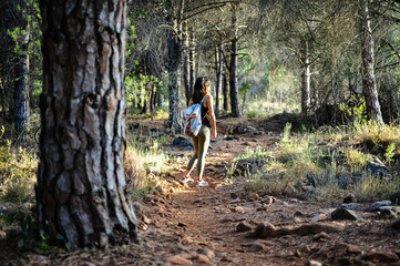 Naklejka na ściany i meble Young woman with backpack walking between trees in the mountain