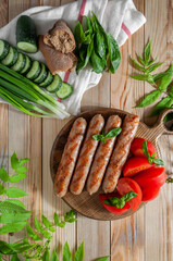 Grilled sausages top view on a wooden round board served with tomatoes, cucumbers and soy, on a light wooden background