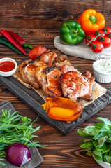 Pork barbecue on a wooden board with grilled pepper, with fresh tomatoes and peppers, herbs and spices on a dark wooden background