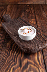 White cream sauce with garlic and hot pepper with a saucepan on a wooden board close-up on a dark background