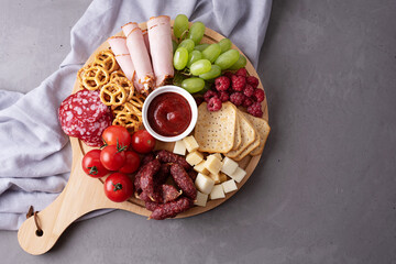 Various snacks on a round charcuterie board on a gray background, party a appetizer.
