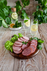 Meat delicacies and sausages on a wooden board on a background of green leaves