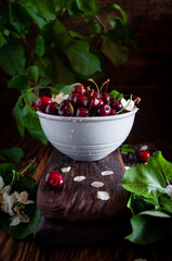 Cherry berries and flowers with water droplets in a blue bowl, on a background of greenery in a low key