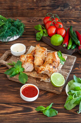 Grilled chicken with herbs, tomatoes, peppers and seasonings on a wooden board on a dark brown background