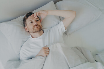 Young tired bearded man lying on bed with open eyes