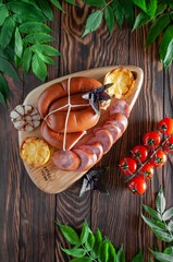 Smoked sausage with grilled lemon, garlic and basil on a wooden board, on a dark background, with cherry tomatoes