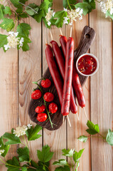 Grilled sausages with baked tomatoes on a dark cutting board with sauce, with summer flowers on a light wooden background